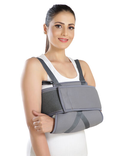 Person wearing a shoulder immobilizer brace with adjustable straps and chest band, providing firm support and restricting arm movement close to the body.